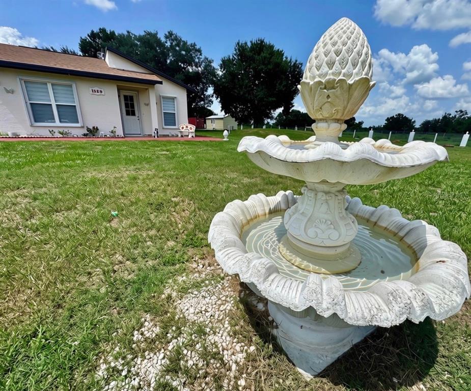 A tiered white fountain stands in the foreground of a grassy yard before a house — 1129 HOPKINS LANE, ZOLFO SPRINGS, FL