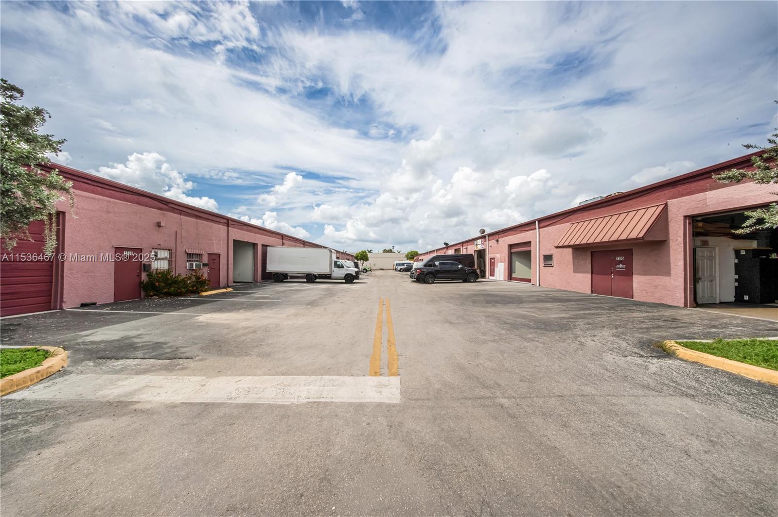 A paved driveway sits between two rows of pink industrial warehouse buildings under a cloudy sky — 1375 NW 65TH AV, Plantation FL 33313, PLANTATION, FL