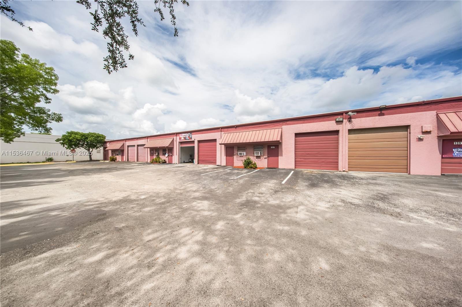 A row of pink industrial warehouse units features multiple roll-up doors and a paved parking lot — 1375 NW 65TH AV, Plantation FL 33313, PLANTATION, FL