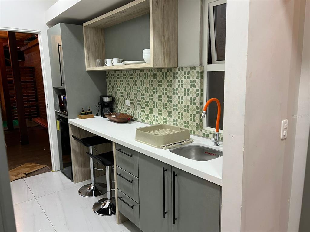 A small kitchen features gray cabinets, a white countertop, and a patterned tile backsplash — 01 RUTA CINTO, MINDO/ECUADOR, PA