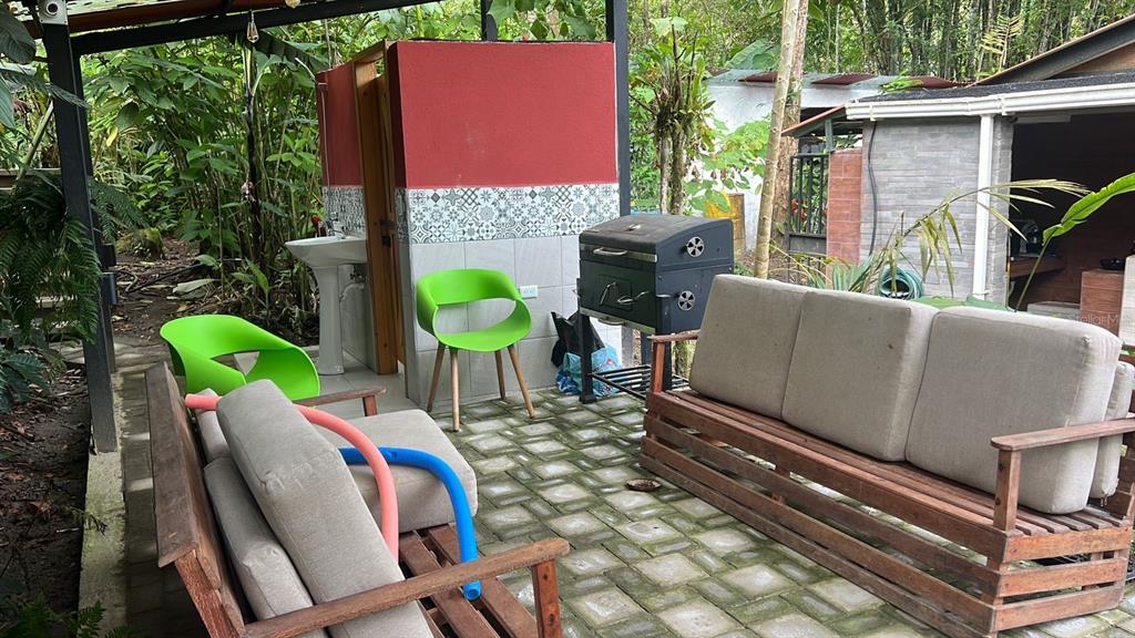 An outdoor patio features wooden furniture, a charcoal grill, and a small sink area — 01 RUTA CINTO, MINDO/ECUADOR, PA