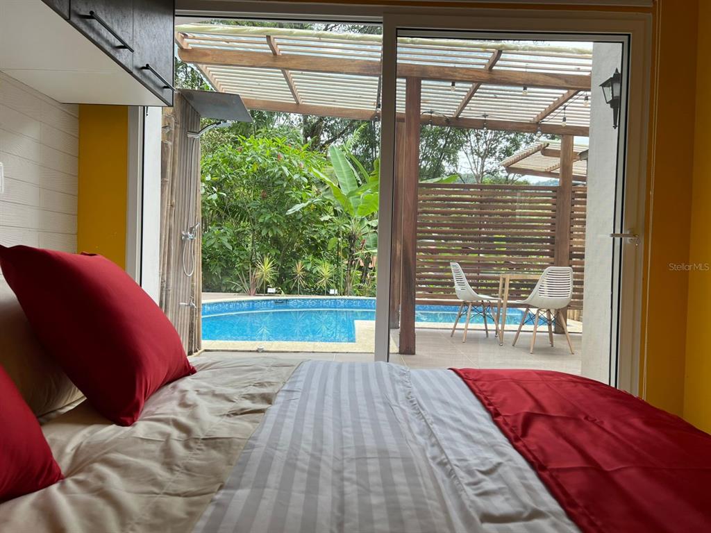 A bedroom with a red-accented bed looks out through sliding glass doors to a pool — 01 RUTA CINTO, MINDO/ECUADOR, PA