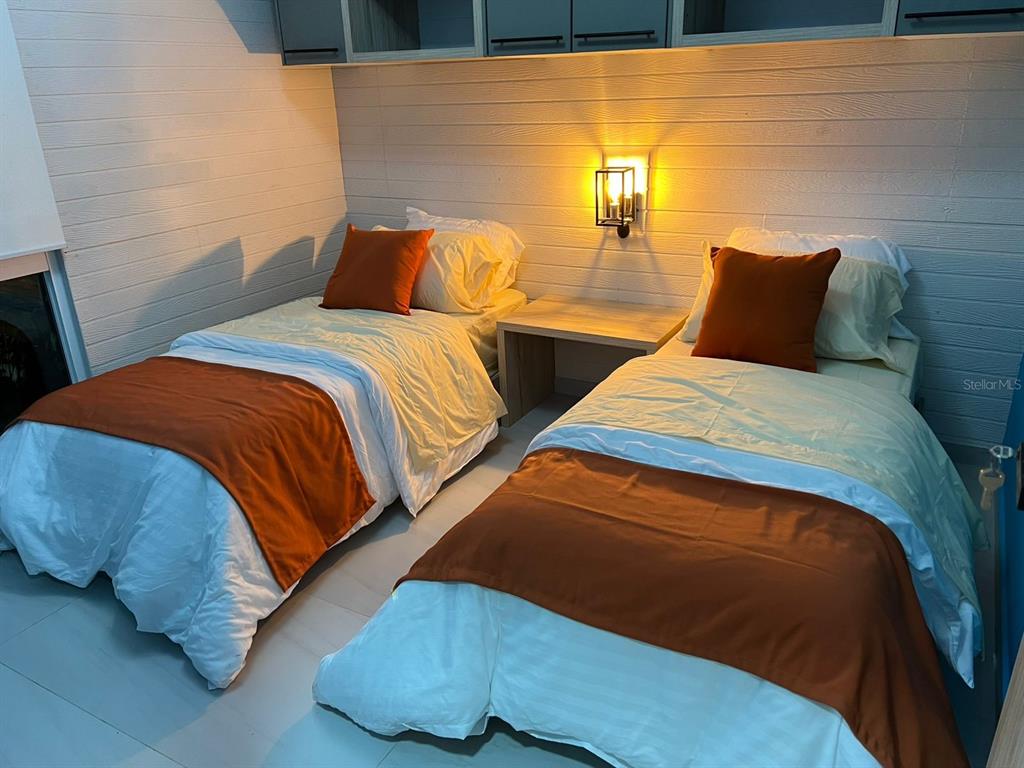 A bedroom features two twin beds with white and orange bedding separated by a nightstand — 01 RUTA CINTO, MINDO/ECUADOR, PA