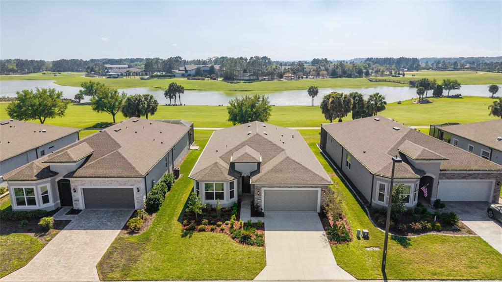 An aerial view shows three suburban houses with driveways facing a golf course and lake — 5740 SW 90TH COURT ROAD, OCALA, FL
