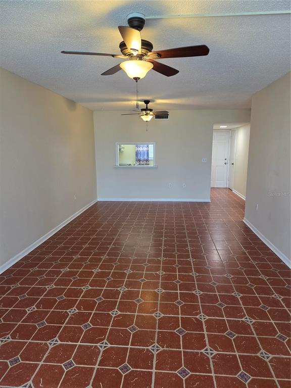 An empty room features terracotta-colored tile flooring, two ceiling fans, and a kitchen pass-through window — 10351 REGAL DRIVE UNIT 3, LARGO, FL