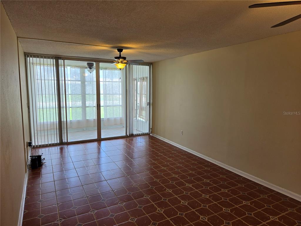 An empty room with brown tiled flooring, beige walls, and sliding glass doors to a patio — 10351 REGAL DRIVE UNIT 3, LARGO, FL