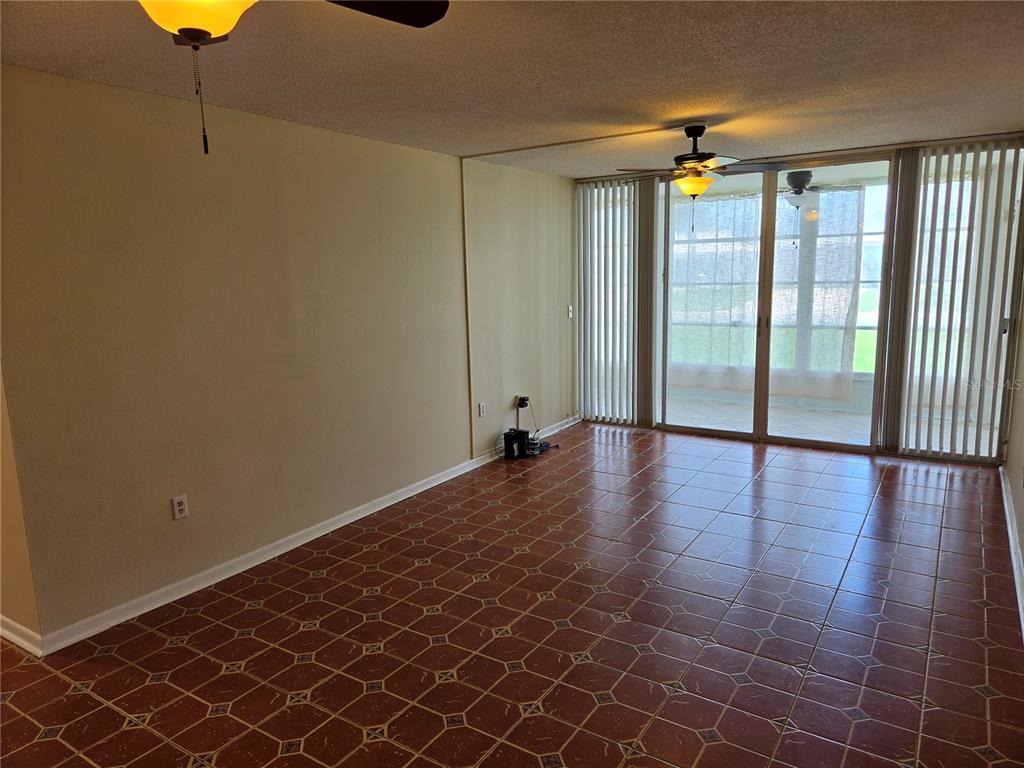 An empty room features reddish-brown tile flooring, beige walls, and sliding glass doors to a patio — 10351 REGAL DRIVE UNIT 3, LARGO, FL