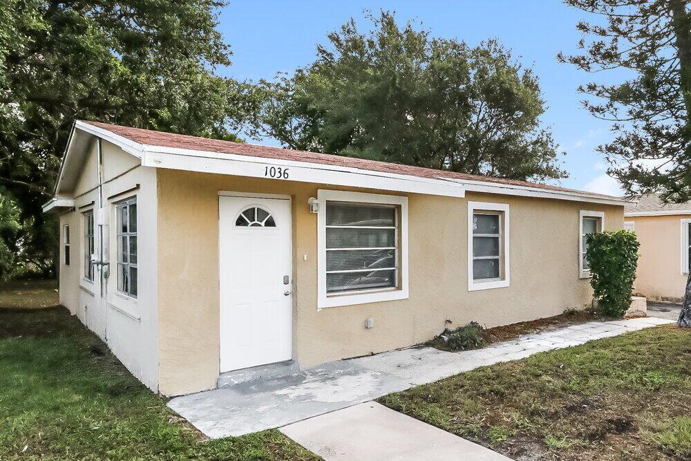 A single-story house with tan stucco siding, a white front door, and a shingled roof — RIVIERA BEACH, FL