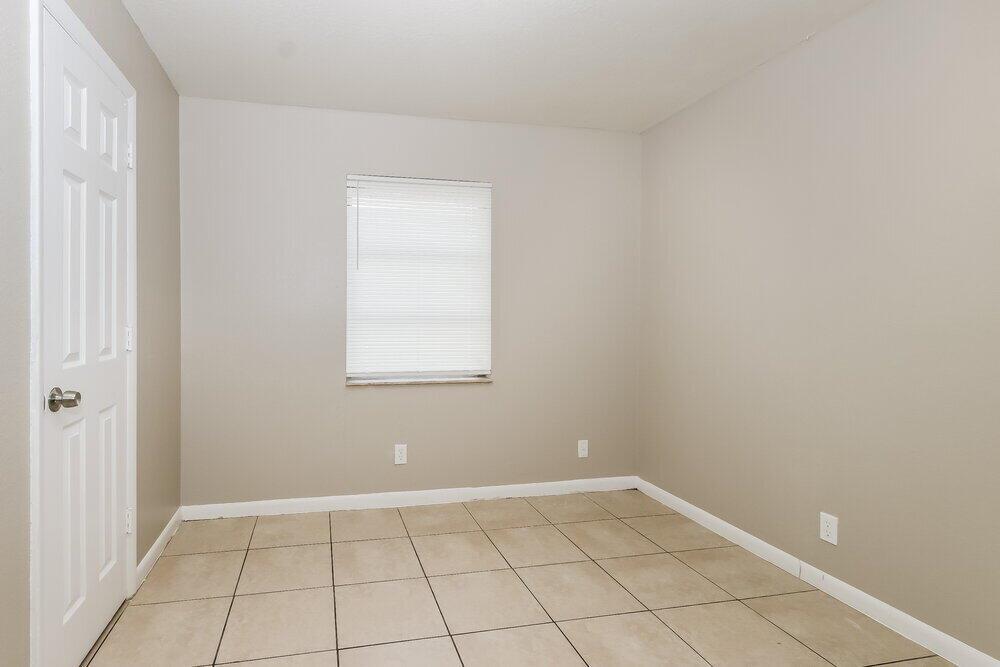 An empty room with beige walls, white trim, a single window, and tiled flooring — RIVIERA BEACH, FL