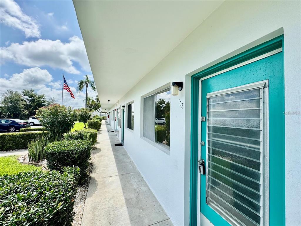 A view of a building exterior walkway with a teal door and a numbered sign — 8305 111TH STREET UNIT 108, SEMINOLE, FL