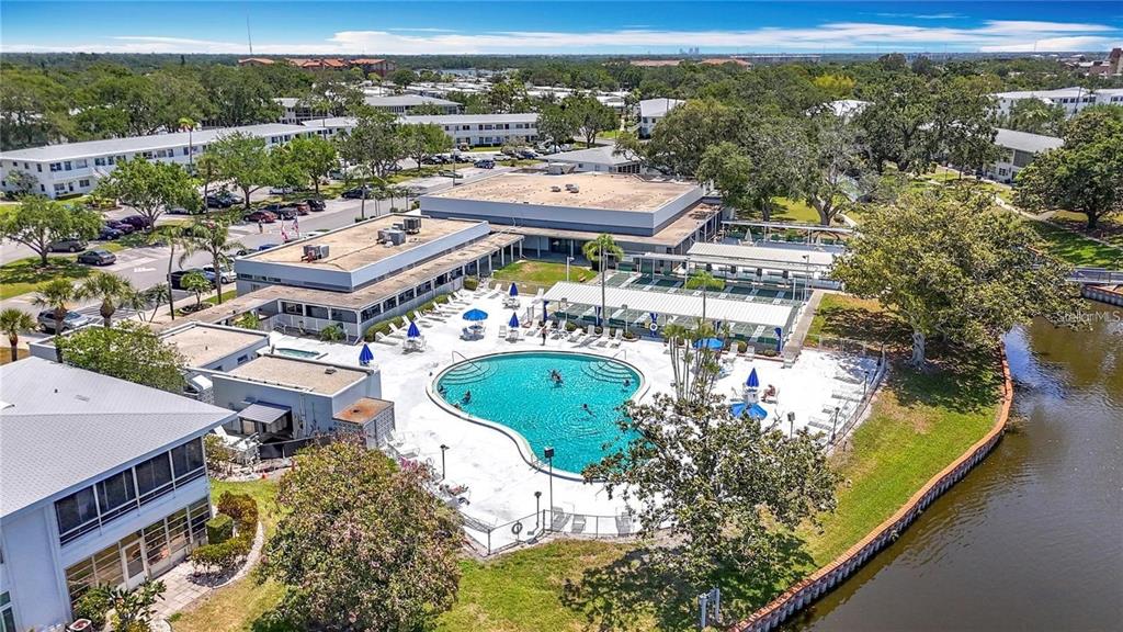 An aerial view shows a community swimming pool surrounded by buildings and a canal — 8305 111TH STREET UNIT 108, SEMINOLE, FL