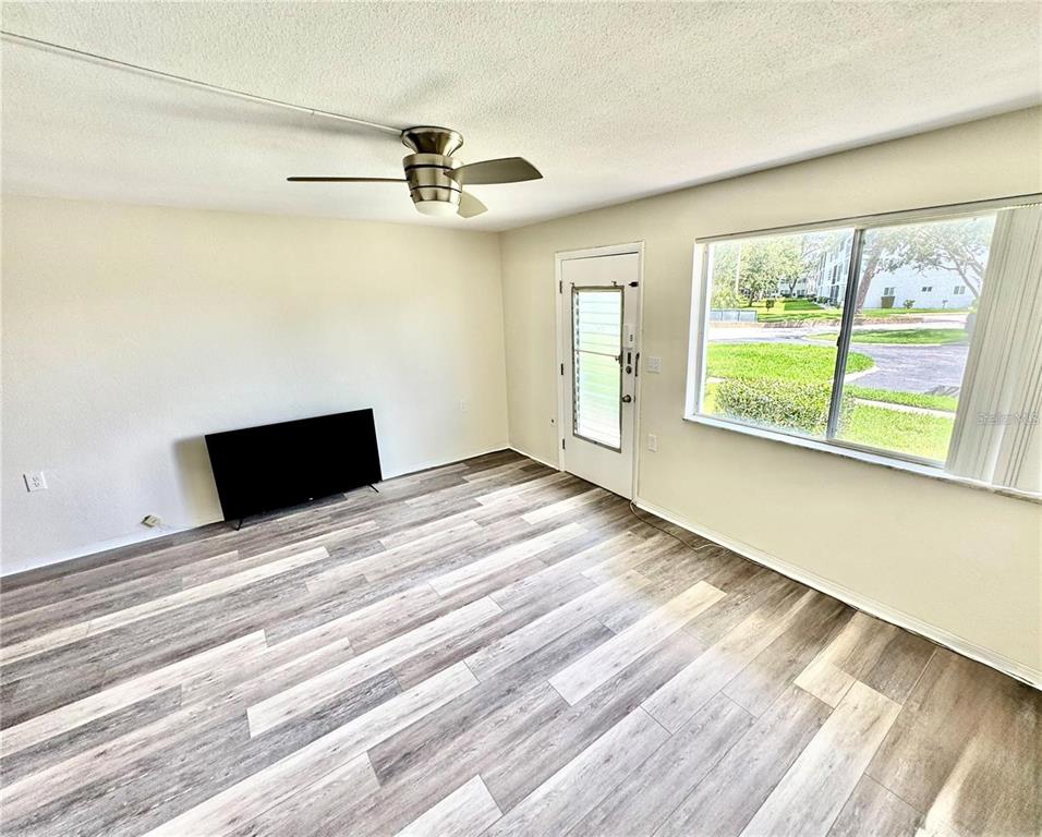 An empty living room features wood-look flooring, a ceiling fan, a television, and a window — 8305 111TH STREET UNIT 108, SEMINOLE, FL