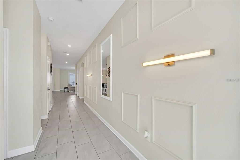 A long hallway features light-colored tile flooring, wall molding panels, and a modern linear light fixture — 2748 BOOKMARK DRIVE, KISSIMMEE, FL