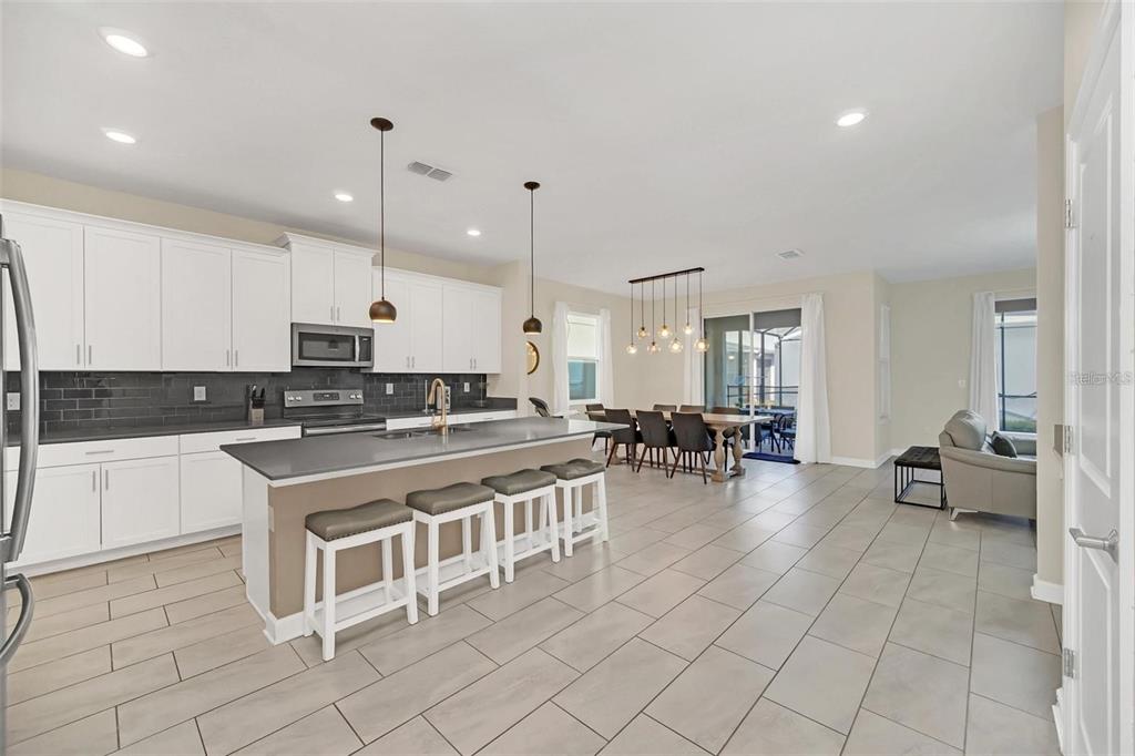 A modern open-concept kitchen and dining area with white cabinets, a large island, and tile flooring — 2748 BOOKMARK DRIVE, KISSIMMEE, FL