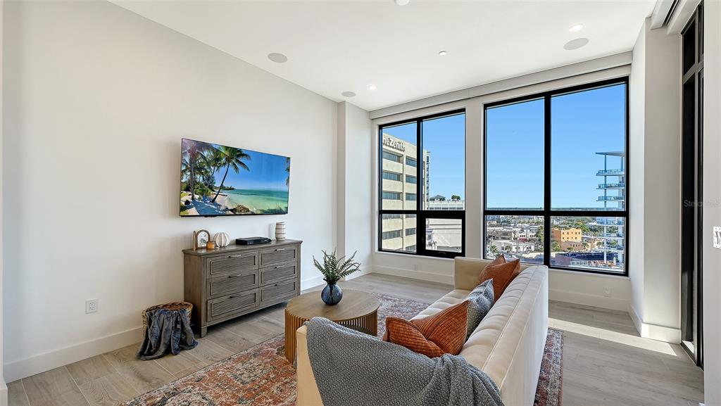 A modern living room features a wall-mounted television, a wooden dresser, and floor-to-ceiling windows — 33 S PALM AVENUE UNIT 904, SARASOTA, FL