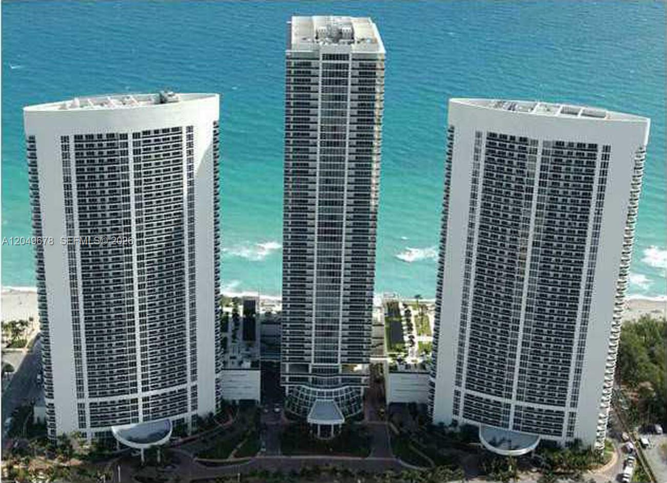 An aerial view shows three tall residential towers situated along a sandy beach and ocean — 1800 S Ocean Dr # 1606, Hallandale Beach FL 33009, HALLANDALE BEACH, FL