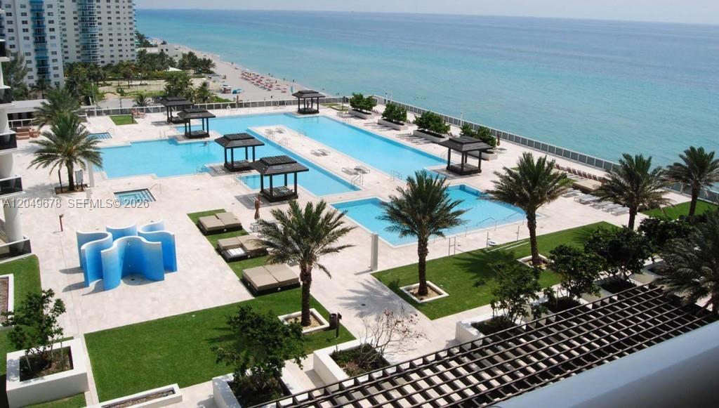 An elevated view of a resort-style pool deck with palm trees overlooking the ocean — 1800 S Ocean Dr # 1606, Hallandale Beach FL 33009, HALLANDALE BEACH, FL