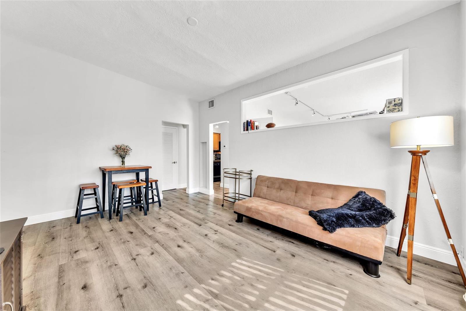 A living room with light wood-look flooring, a tan sofa, a dining set, and a floor lamp — 805 NE 17th Avenue # 4, Fort Lauderdale FL 33304, FORT LAUDERDALE, FL