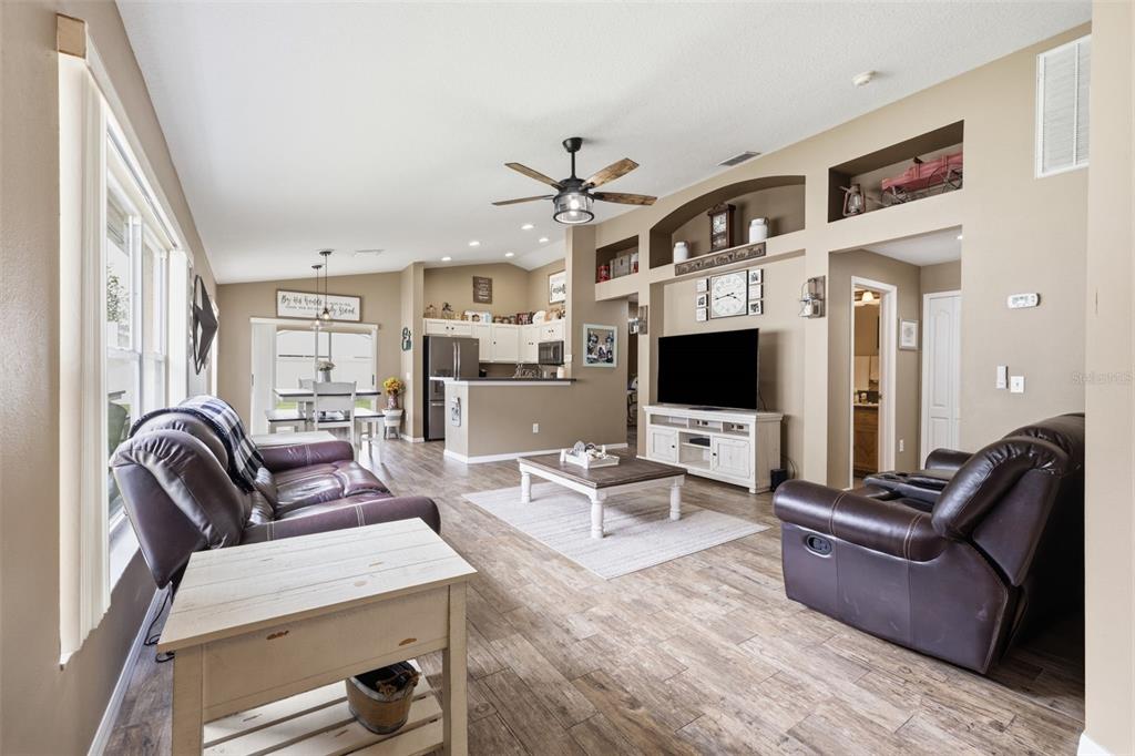 A living room features wood-look tile flooring, a vaulted ceiling, and an open kitchen area — 23814 CORAL RIDGE LANE, LAND O LAKES, FL