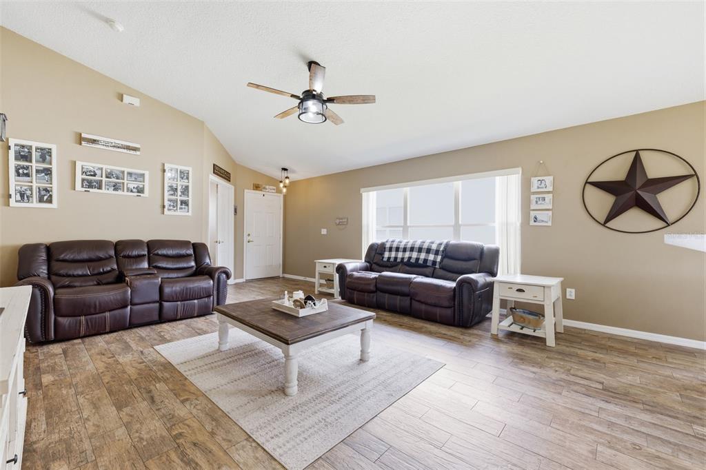 A living room features two brown leather sofas, a wooden coffee table, and wood-look flooring — 23814 CORAL RIDGE LANE, LAND O LAKES, FL