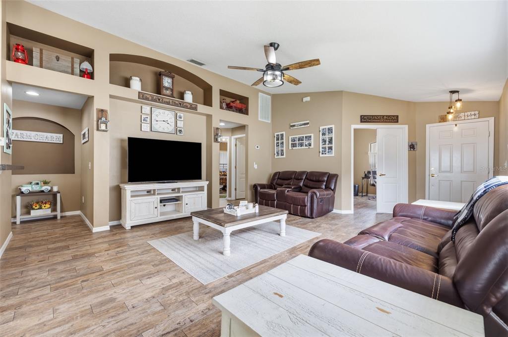 A living room features brown leather sofas, a television on a white console, and wood-look flooring — 23814 CORAL RIDGE LANE, LAND O LAKES, FL