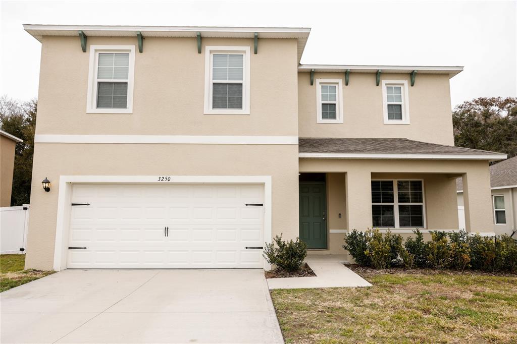 A two-story house with a beige stucco exterior, a two-car garage, and a front porch — 3250 BLUE CRAB DRIVE, TAVARES, FL