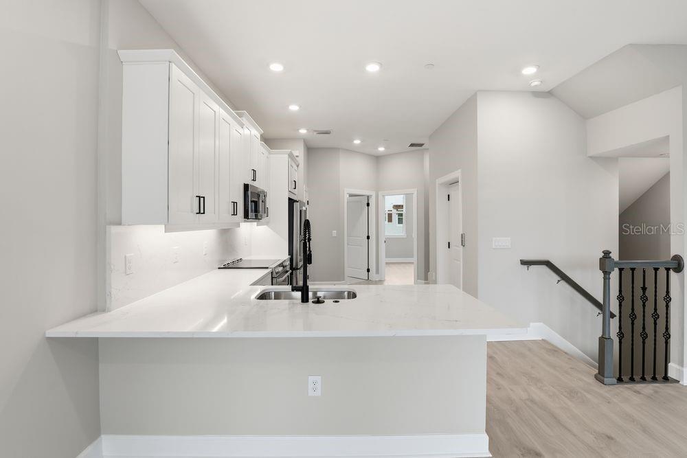 A modern kitchen features white cabinets, quartz countertops, and a breakfast bar overlooking stairs — 1624 COMPASS POINTE COURT UNIT 203, PUNTA GORDA, FL