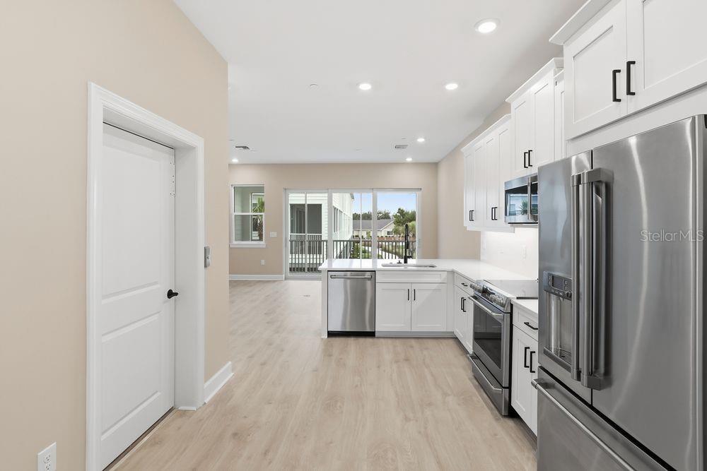 A modern kitchen with white cabinets, stainless steel appliances, and light wood-look flooring — 1624 COMPASS POINTE COURT UNIT 203, PUNTA GORDA, FL