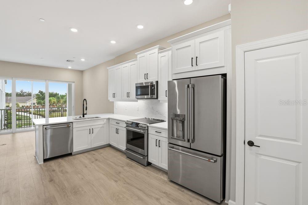 A modern kitchen features white cabinets, stainless steel appliances, and light wood-look flooring — 1624 COMPASS POINTE COURT UNIT 203, PUNTA GORDA, FL