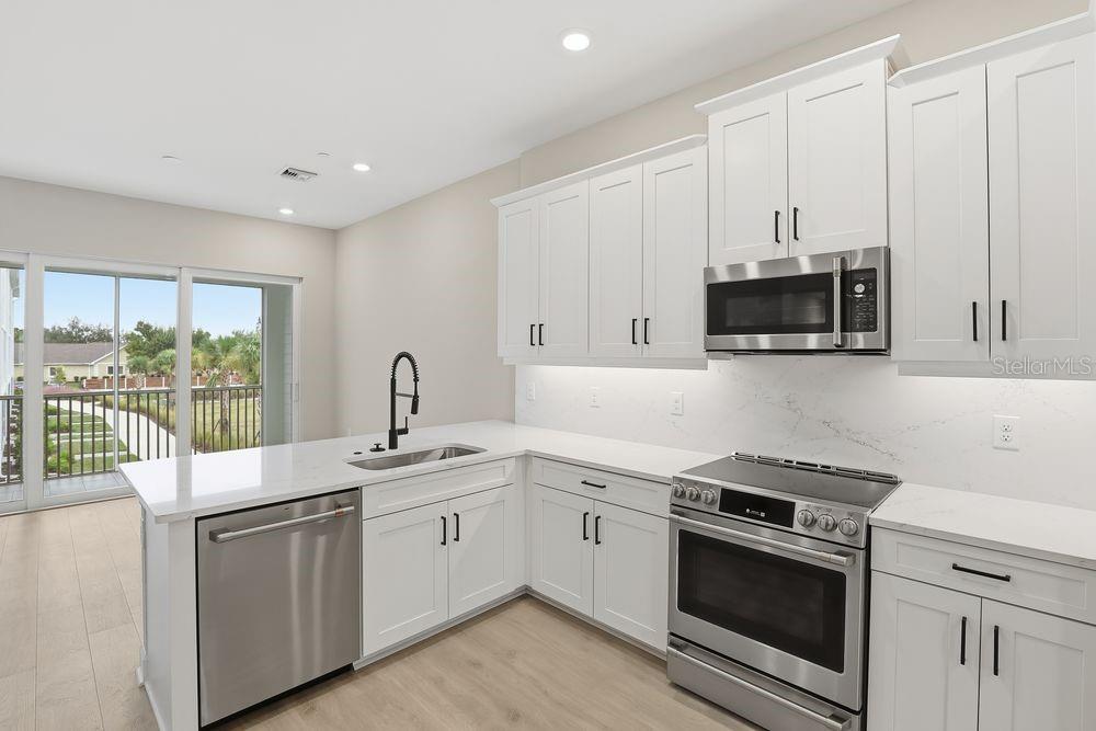 A modern kitchen features white cabinets, stainless steel appliances, and quartz countertops with a sink — 1624 COMPASS POINTE COURT UNIT 203, PUNTA GORDA, FL