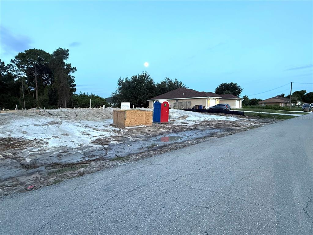 A vacant residential lot features a portable toilet and a wooden box on sandy ground — 104 HOMER AVENUE S, LEHIGH ACRES, FL