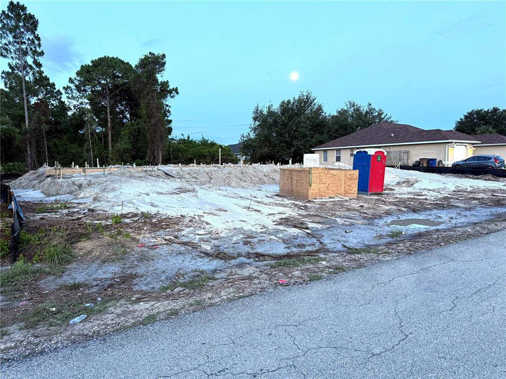 A construction site features a prepared foundation, a portable toilet, and a wooden enclosure — 104 HOMER AVENUE S, LEHIGH ACRES, FL