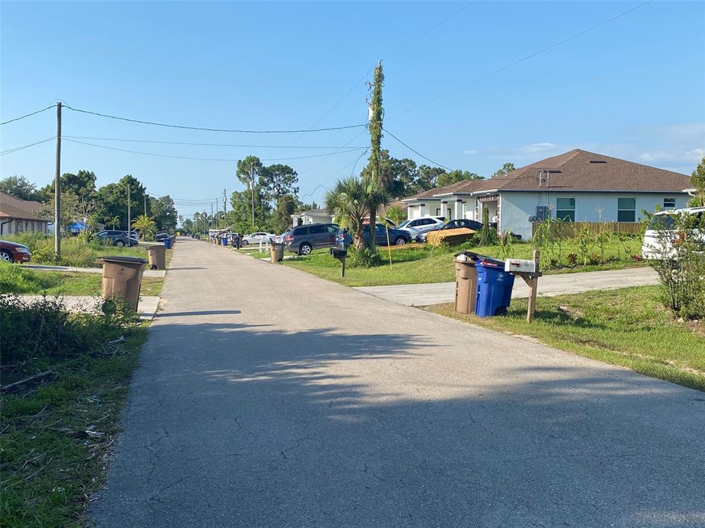 A paved residential street lined with houses, parked cars, and trash bins under a clear sky — 104 HOMER AVENUE S, LEHIGH ACRES, FL
