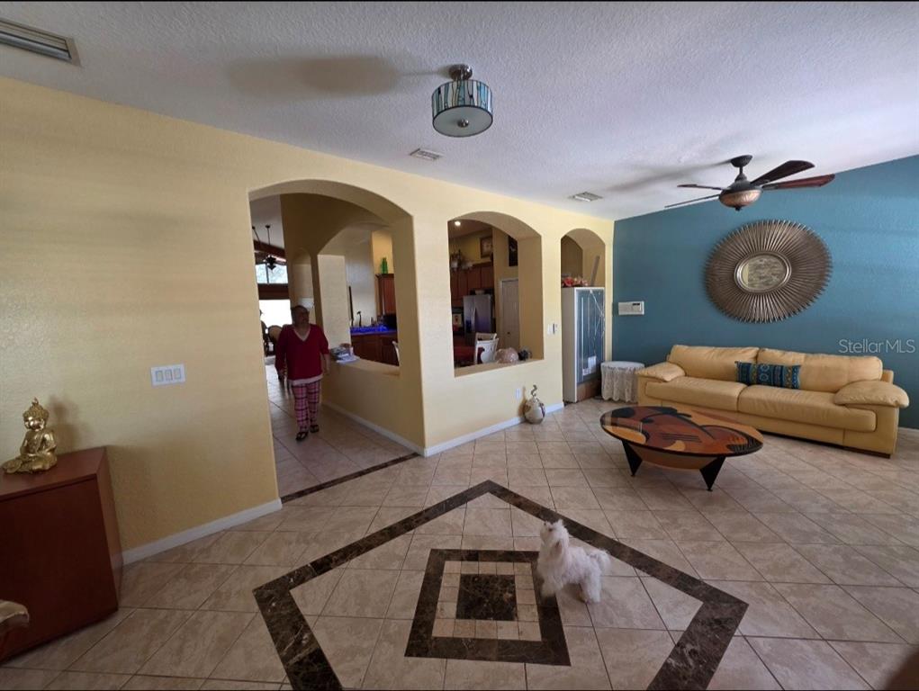 A living room with tile flooring, a yellow sofa, and arched openings to the kitchen — 12435 ADVENTURE DRIVE, RIVERVIEW, FL