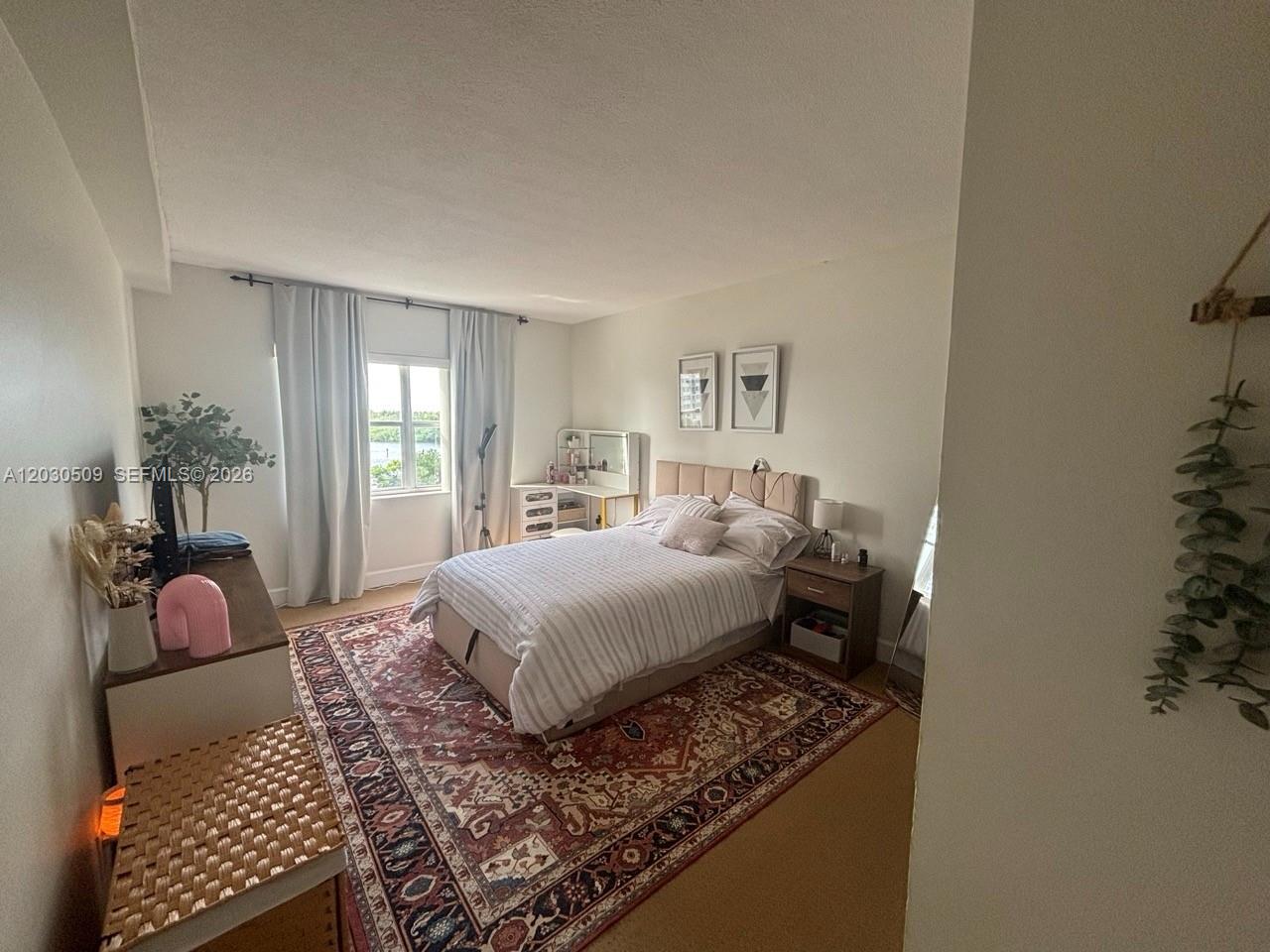 A bedroom features a bed, a patterned rug, a vanity, and a window with curtains — 400 Kings Point Dr # 622, Sunny Isles Beach FL 33160, SUNNY ISLES BEACH, FL