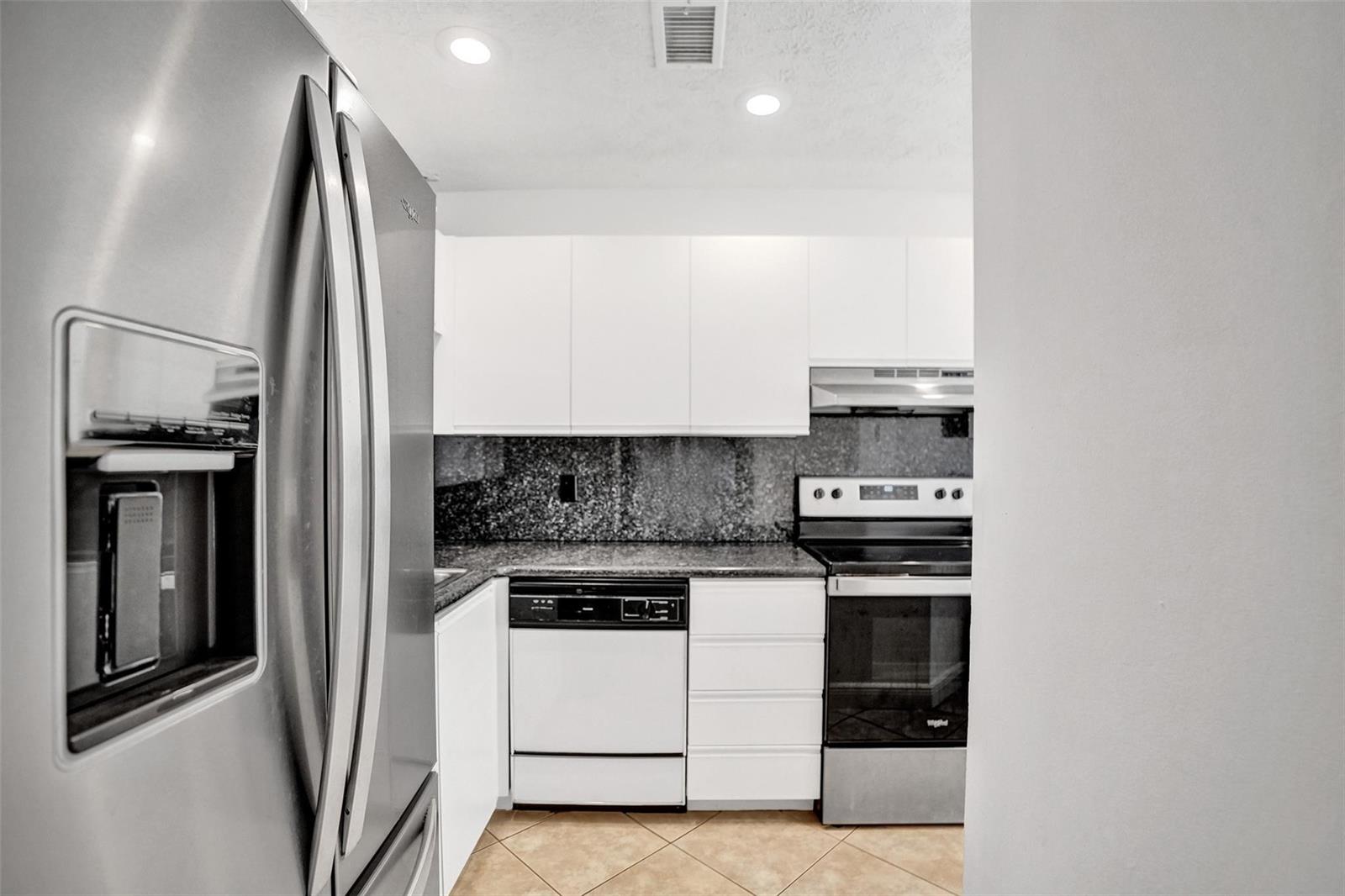 A kitchen features white cabinets, granite countertops, stainless steel appliances, and light-colored tile flooring — 1415 Miami Road # B, Fort Lauderdale FL 33316, FORT LAUDERDALE, FL