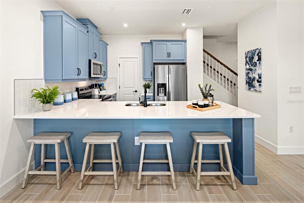 A kitchen features blue cabinets, a white island with four stools, and stainless steel appliances — 5164 GREENSHADE GROVE AVENUE, APOPKA, FL
