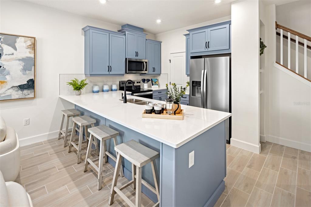 A kitchen features blue cabinets, a white quartz island with bar seating, and tile flooring — 5164 GREENSHADE GROVE AVENUE, APOPKA, FL