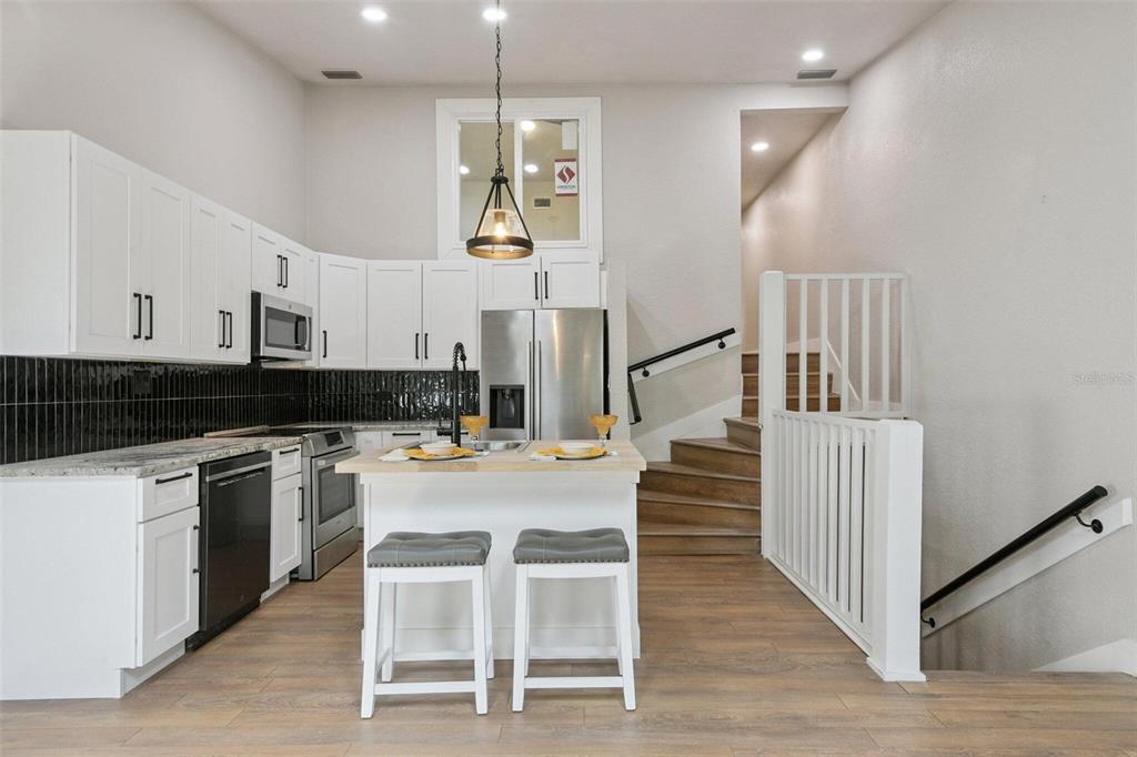 A kitchen features white cabinets, a black tile backsplash, a central island, and adjacent stairs — 6436 92ND PLACE N UNIT 1005, PINELLAS PARK, FL