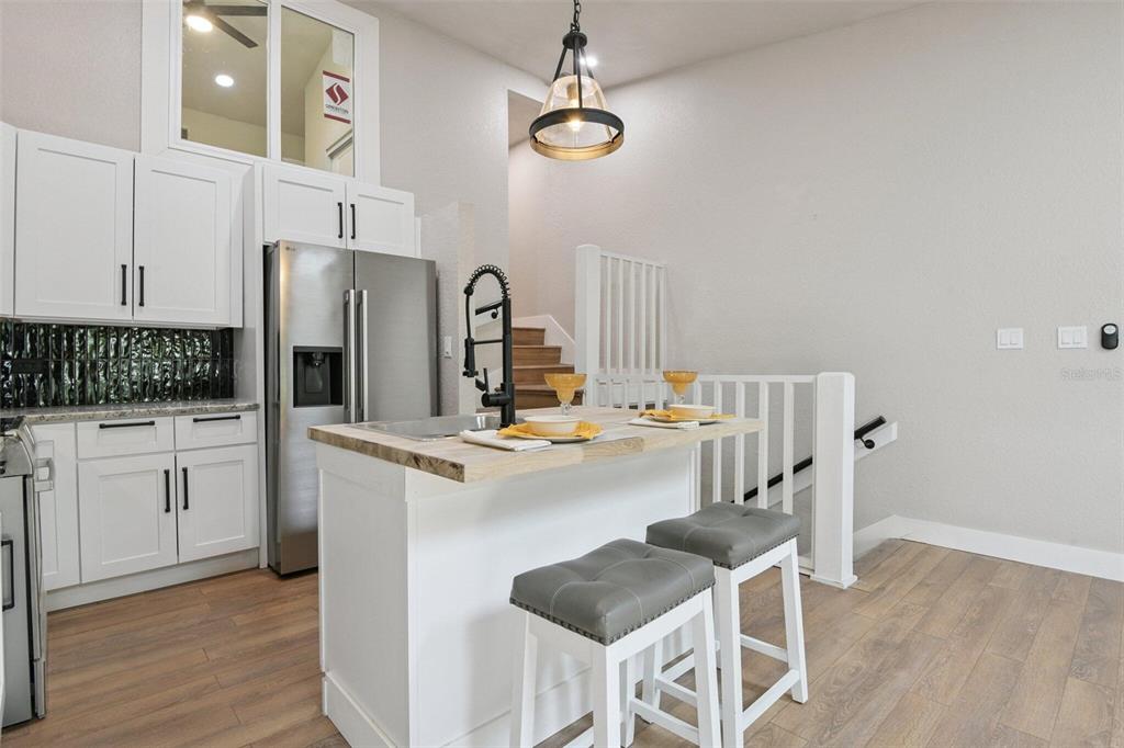 A kitchen features white cabinets, a stainless steel refrigerator, a wooden island, and bar stools — 6436 92ND PLACE N UNIT 1005, PINELLAS PARK, FL