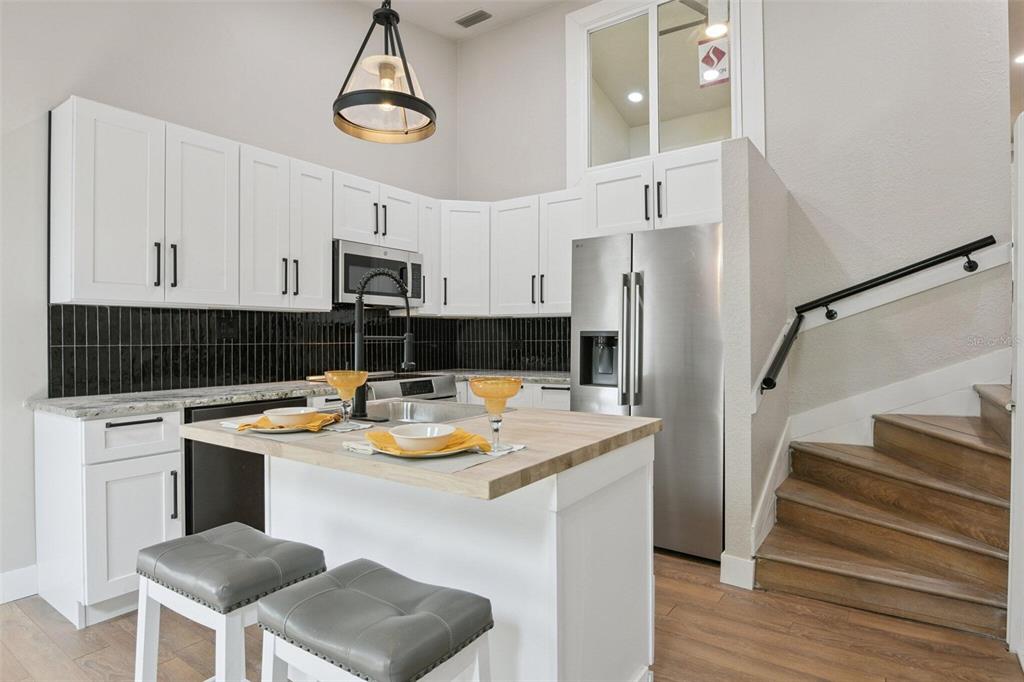 A kitchen with white cabinets, a wood-topped island, stainless steel appliances, and adjacent wooden stairs — 6436 92ND PLACE N UNIT 1005, PINELLAS PARK, FL