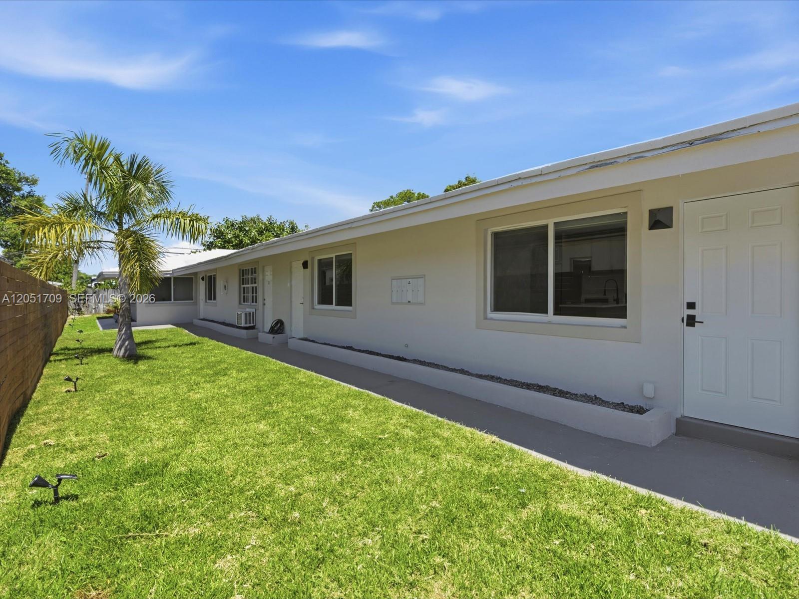 A single-story apartment building exterior features a grassy yard, a palm tree, and white doors — 1129 NE 16th Ave # 1, Fort Lauderdale FL 33304, FORT LAUDERDALE, FL