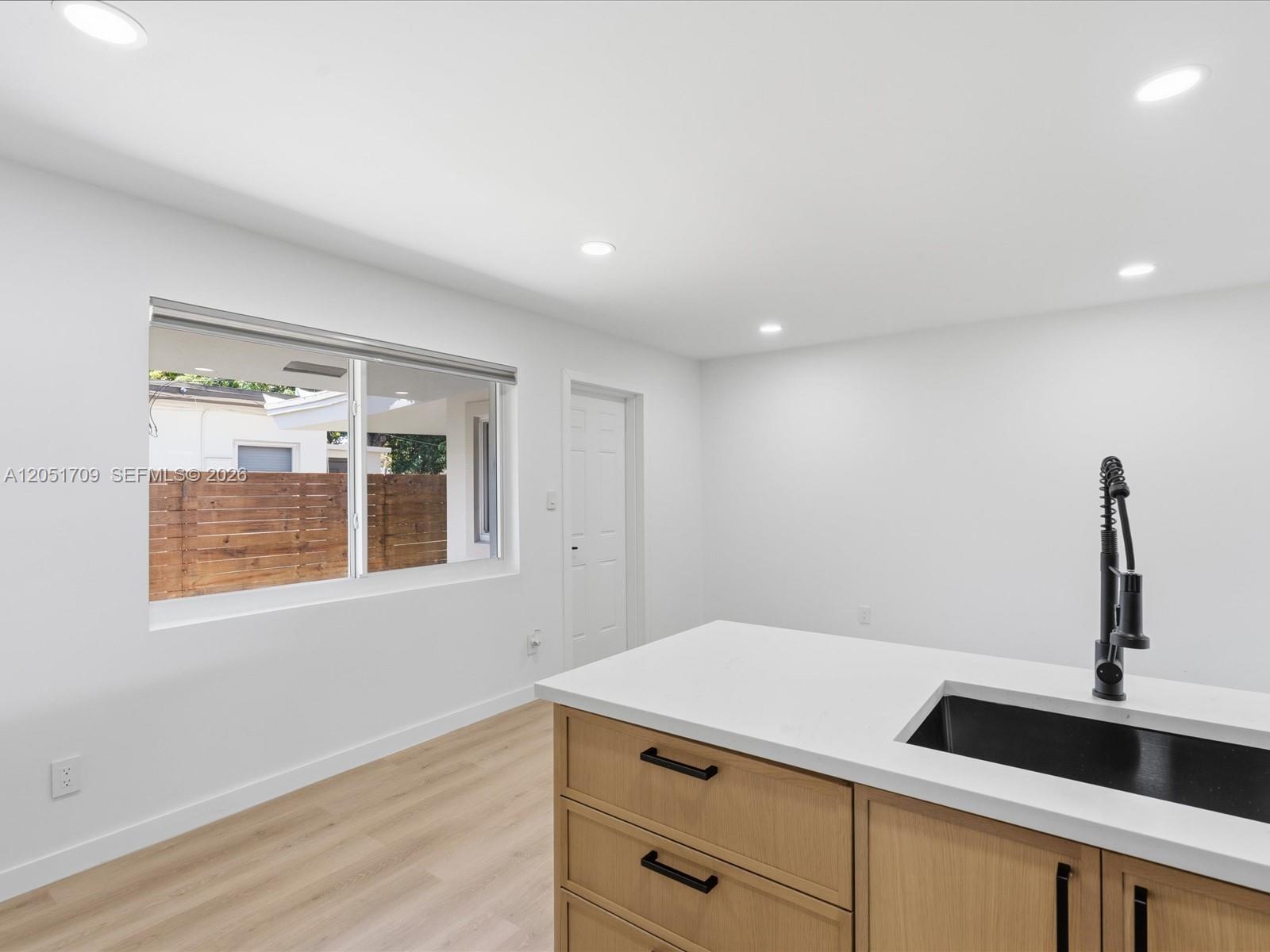 A kitchen island with a black sink and faucet sits in a bright, minimalist room — 1129 NE 16th Ave # 1, Fort Lauderdale FL 33304, FORT LAUDERDALE, FL