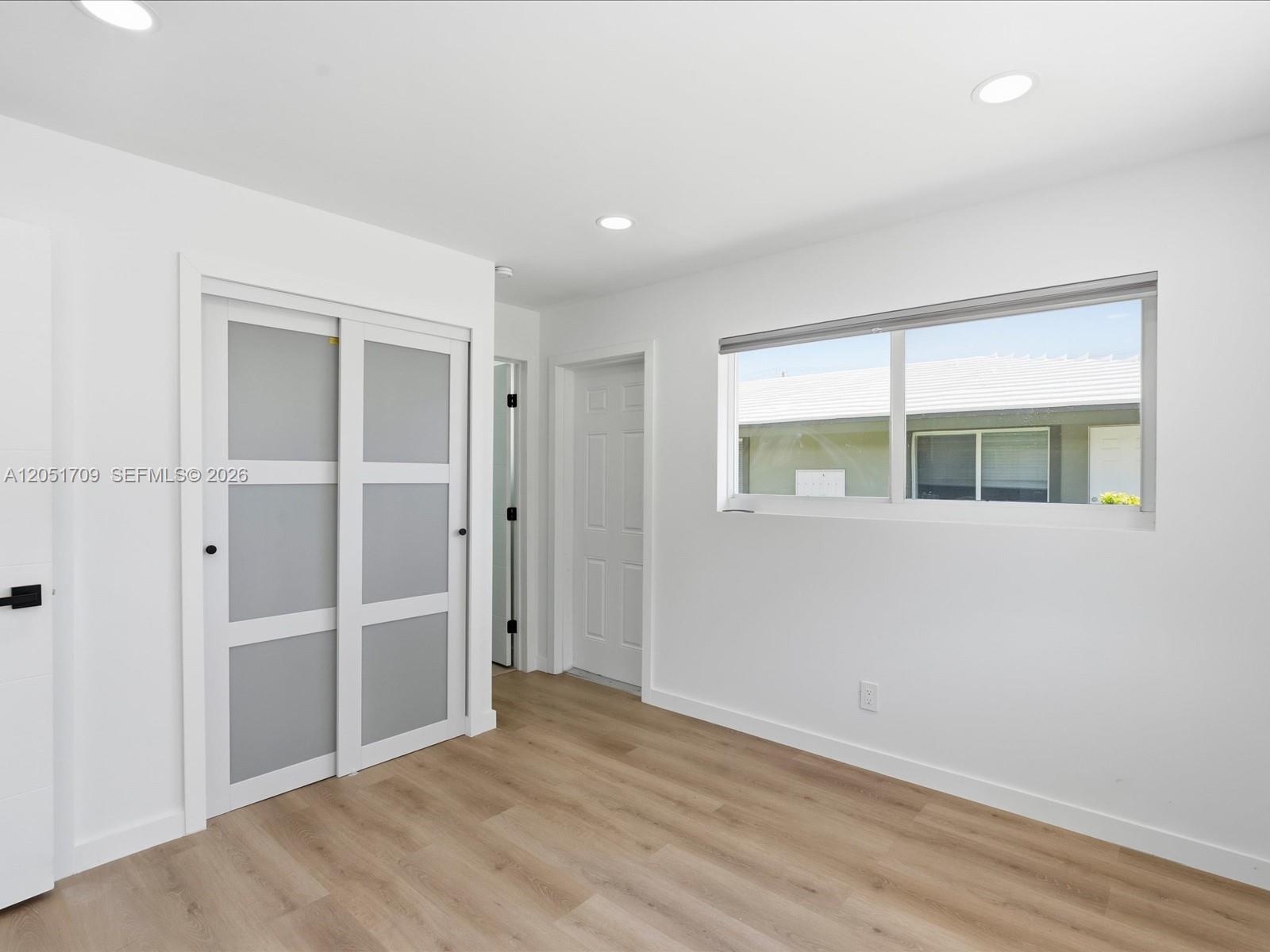 This bedroom features white walls, light wood-look flooring, a sliding closet, and a window — 1129 NE 16th Ave # 1, Fort Lauderdale FL 33304, FORT LAUDERDALE, FL