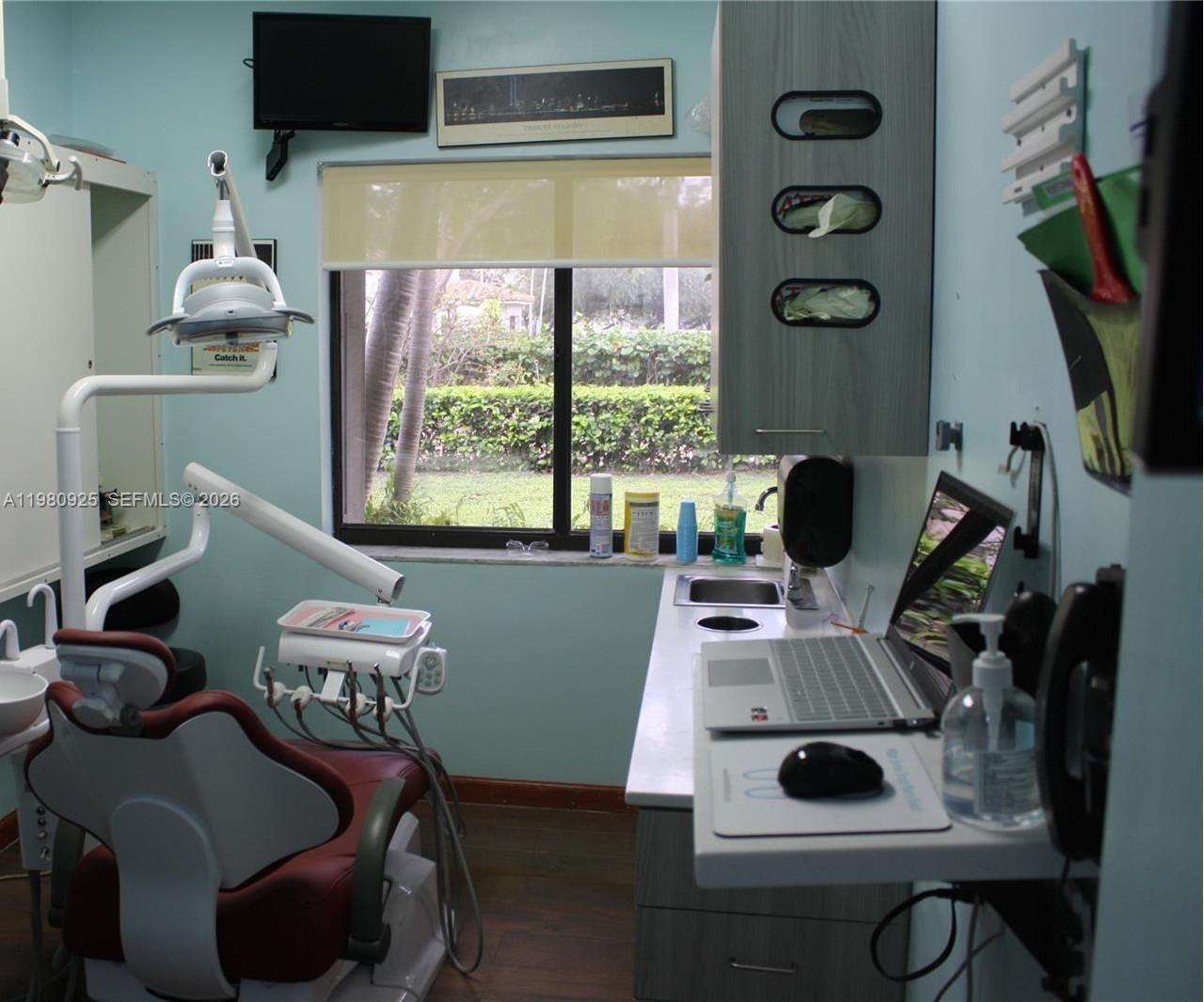 A dental examination room features a patient chair, medical equipment, a laptop, and a window — 1235 Alton Rd, Miami Beach FL 33139, MIAMI BEACH, FL
