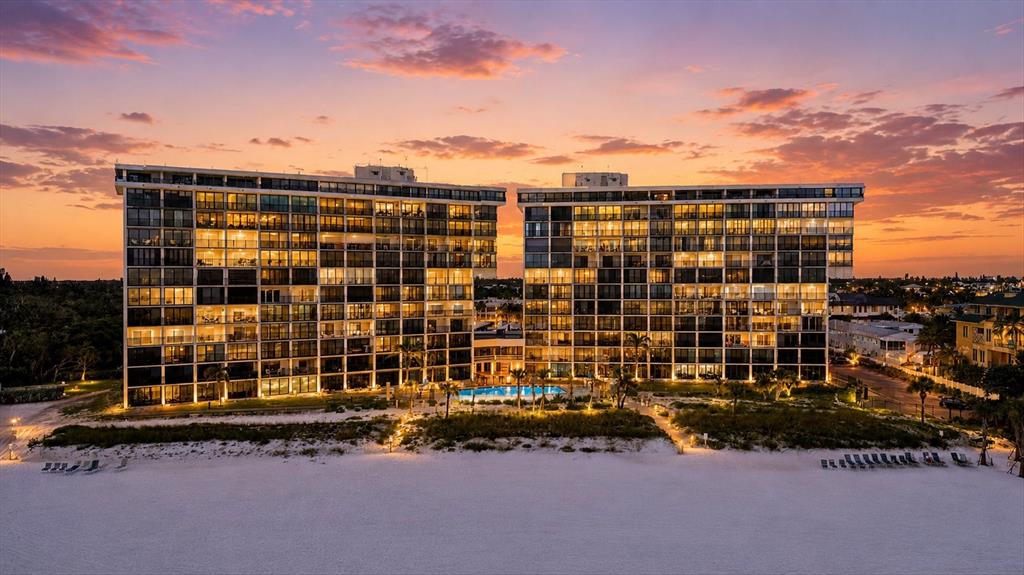 A balcony with two blue chairs and a wine set overlooks a sunset beach view — 20 WHISPERING SANDS DRIVE UNIT 501, SARASOTA, FL