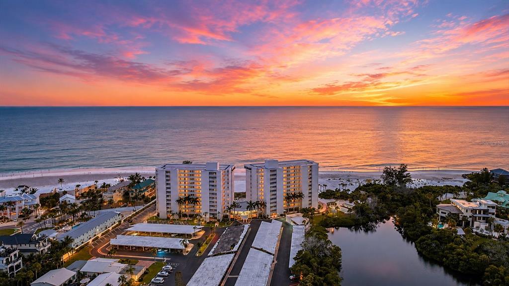 An aerial view shows two high-rise buildings situated on a beach at sunset — 20 WHISPERING SANDS DRIVE UNIT 501, SARASOTA, FL