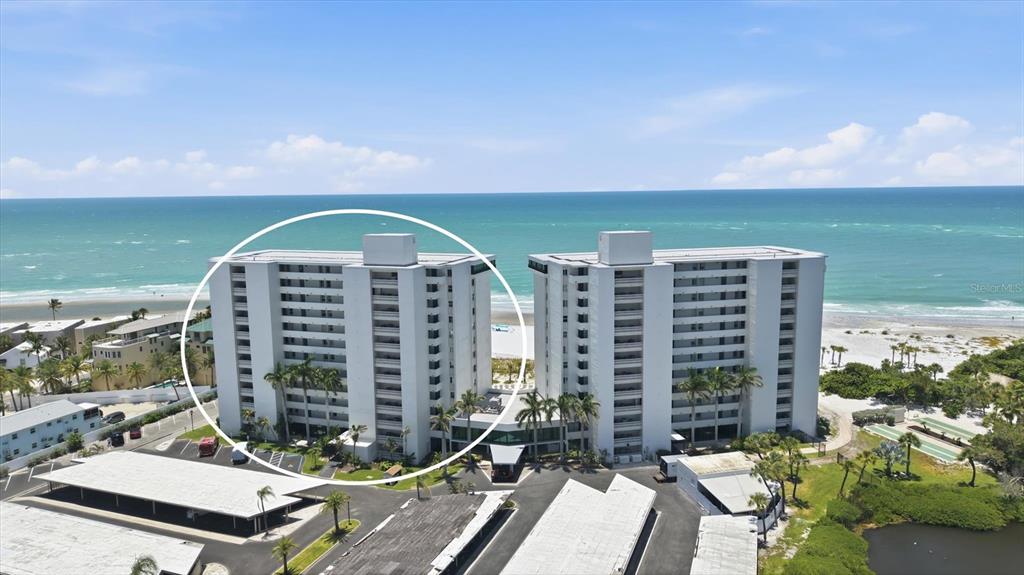 An aerial view shows two white high-rise residential buildings situated along a sandy beach — 20 WHISPERING SANDS DRIVE UNIT 501, SARASOTA, FL