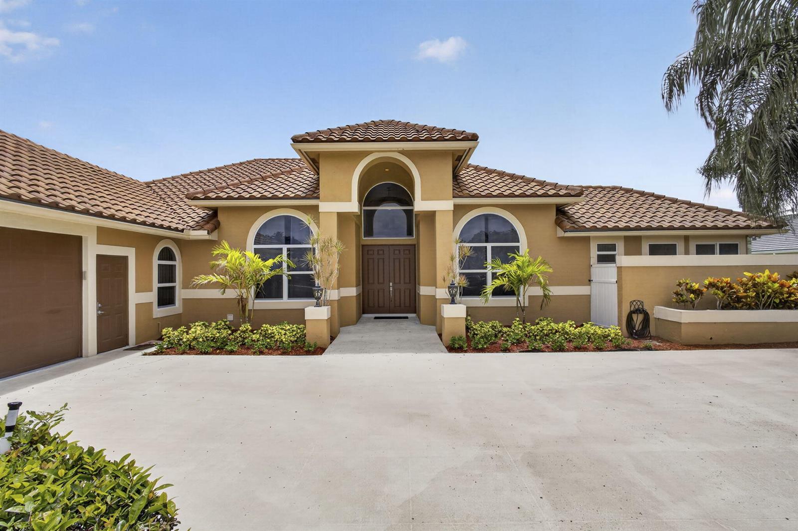 A single-story house with a tan stucco exterior, arched windows, and a brown tile roof — 8030 Woodsmuir Drive, Palm Beach Gardens FL 33412, PALM BEACH GARDENS, FL