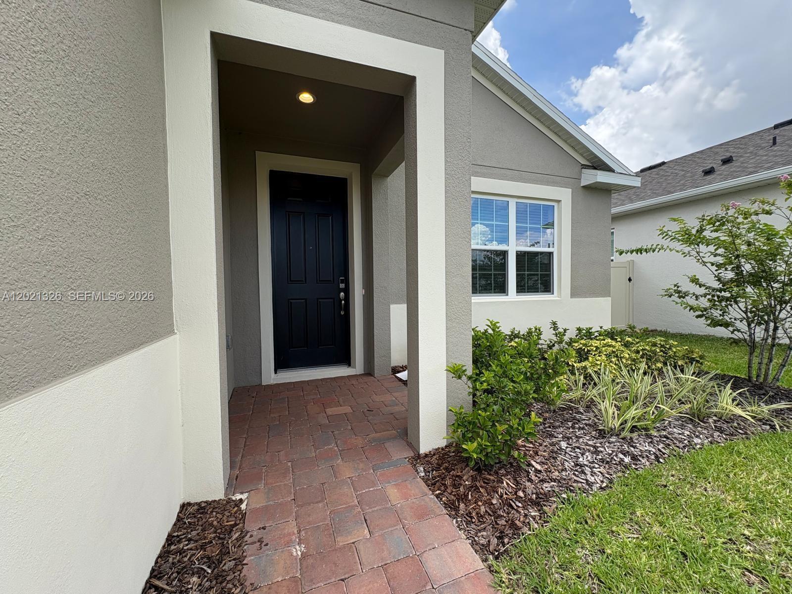 A paved walkway leads to the front entrance of a house with a dark door — 366 SWITCHGRASS LOOP # 366, Other City - In The State Of Florida FL 34715, OTHER CITY - IN THE STATE OF FLORIDA, FL